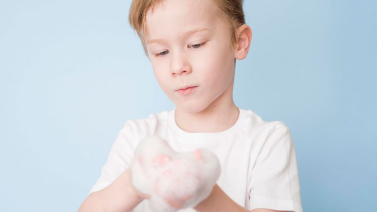 Criança com camisa branca com a as duas mãos ensaboadas.