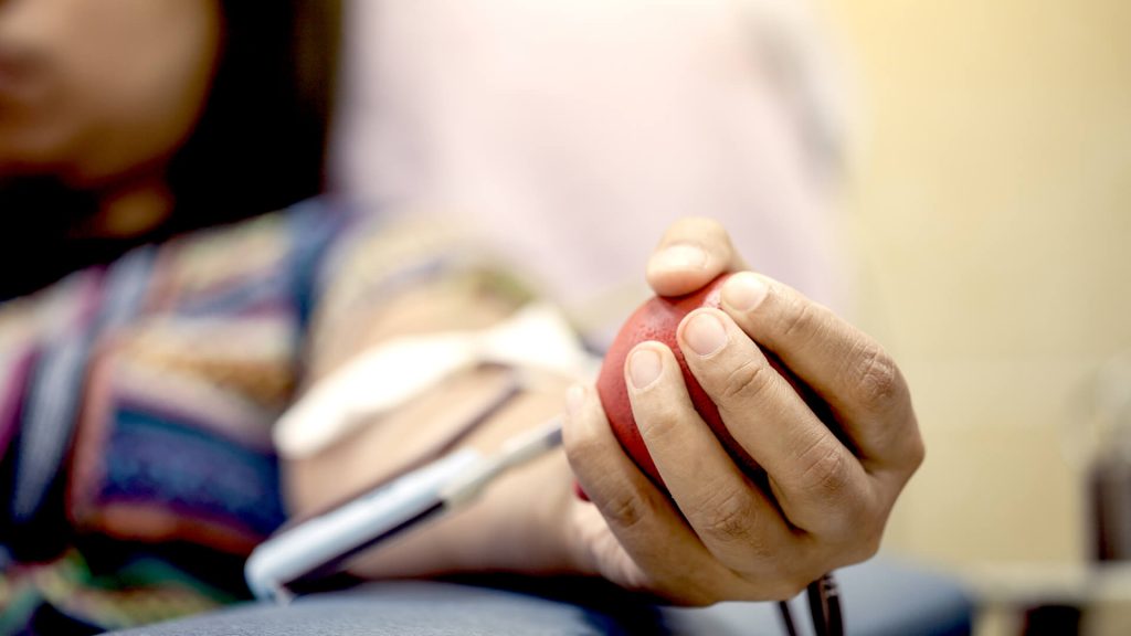 Mulher sentada em uma poltrona para doar sangue, segurando uma bola vermelha na mão esquerda